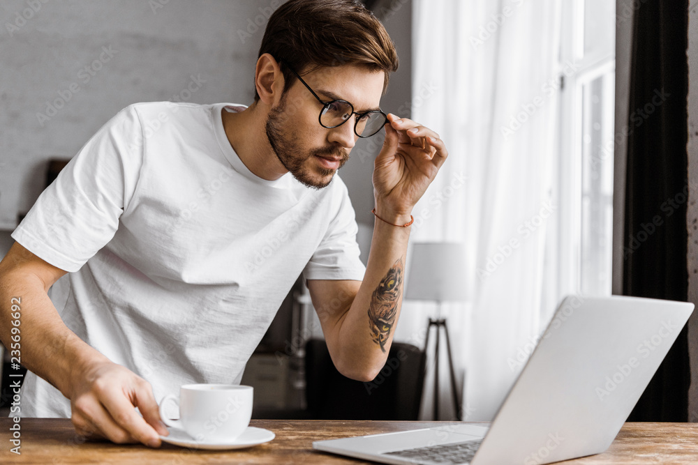 stressed young man with coffee looking at laptop screen at home stressed young man with coffee looking at laptop screen at home