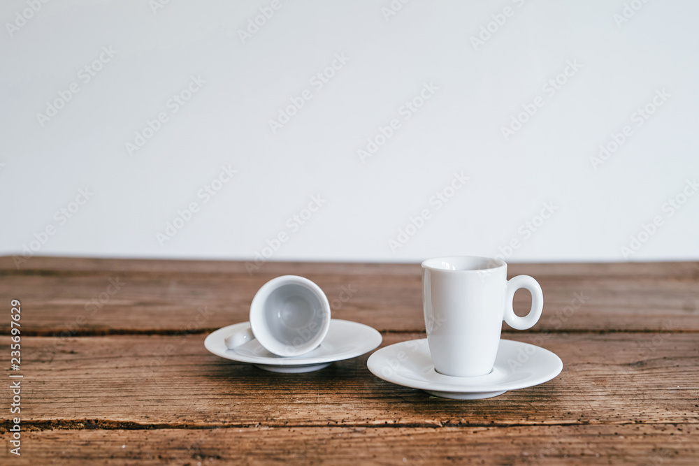 2 Espresso Tassen leer liegend auf Unterteller Holztisch Hintergrund weiß 2 Espresso Tassen leer liegend auf Unterteller Holztisch Hintergrund weiß