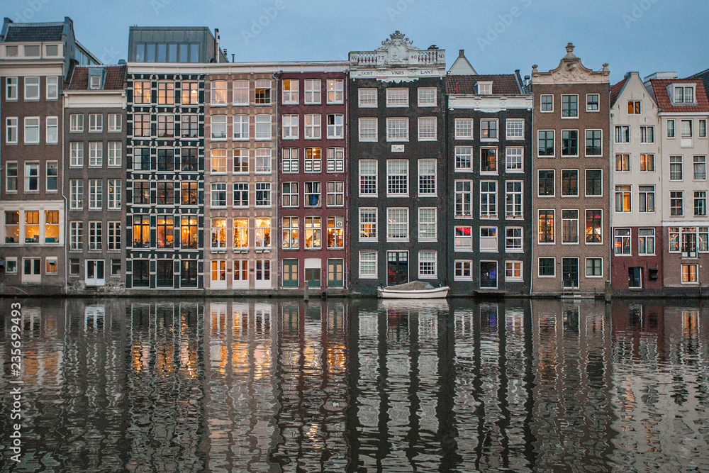 Amsterdam canal Singel with typical dutch houses illuminated in the evening. Illuminated buildings reflection in the Amsterdam canal. 