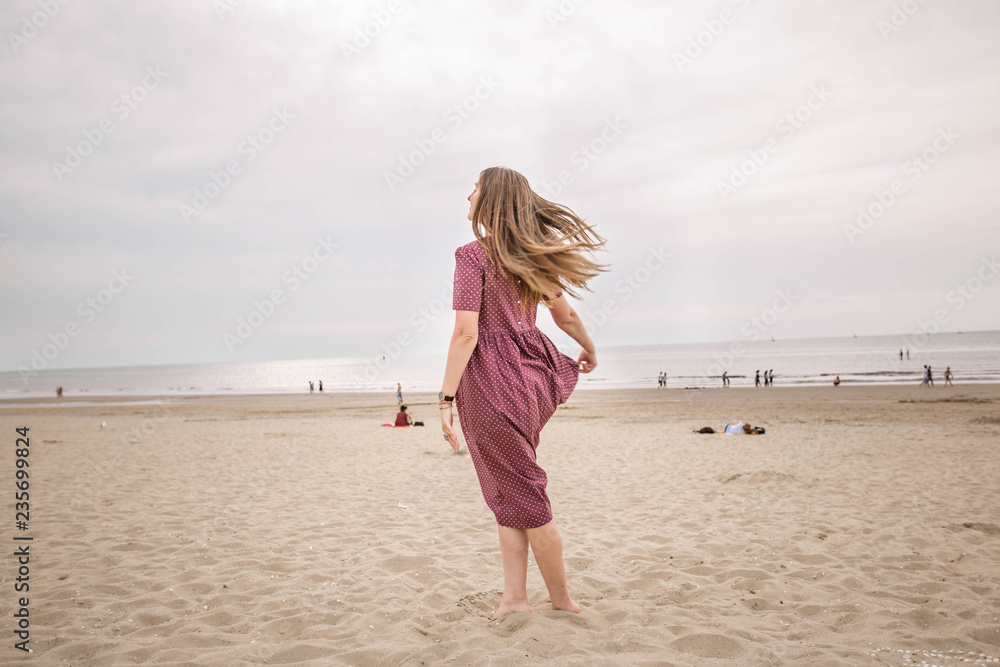 Young beautiful brunette woman in burgundy dress dance on the Scheveningen Beach in The Hague, The Netherlands. Young beautiful brunette woman in burgundy dress dance on the Scheveningen Beach in The Hague, The Netherlands.