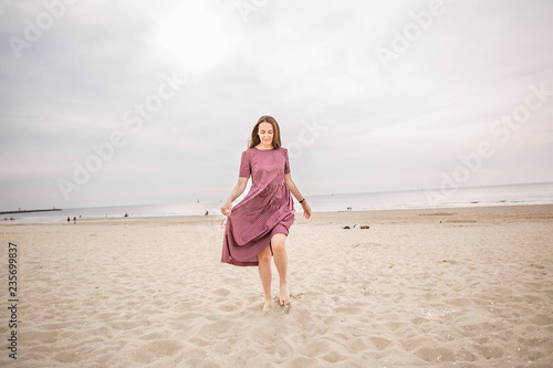Young beautiful brunette woman in burgundy dress dance on the Scheveningen Beach in The Hague, The Netherlands.
