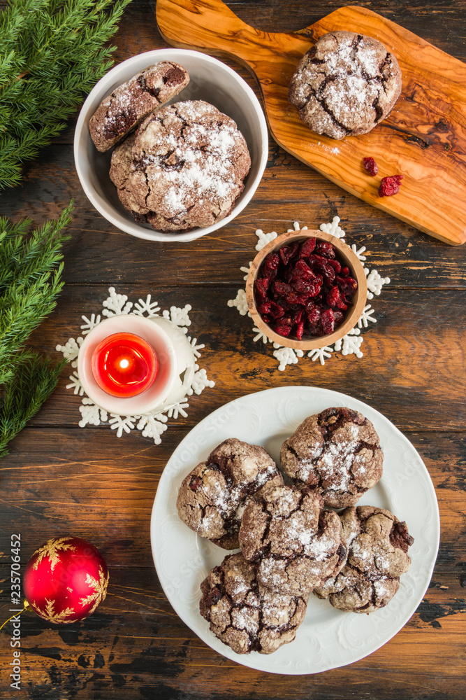 Cracked chocolate cookies with cranberries on white plate on wooden rustic table. Christmas decoration, top view Cracked chocolate cookies with cranberries on white plate on wooden rustic table. Christmas decoration, top view