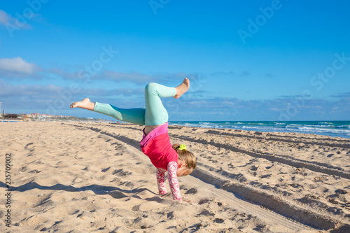 Foto four years old little girl trying to do handstand or somersault on sandy Beach L