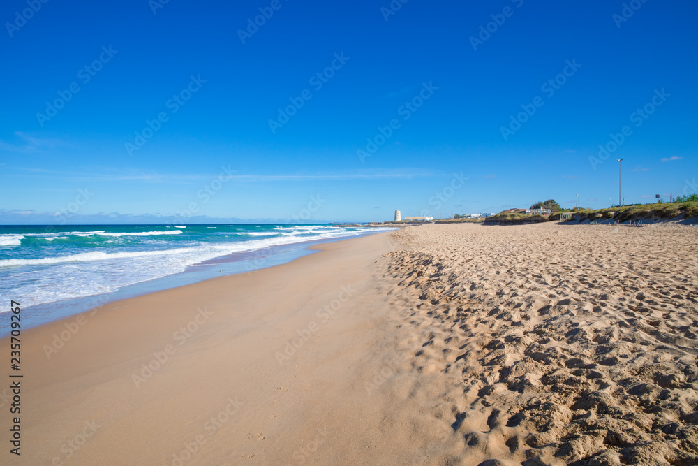 seaside of beautiful and lonely Palmar Beach with sand, turquoise ocean water and ancient tower in the horizon. In Vejer village (Cadiz, Andalusia, Spain)