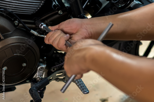 Image is Close up,People are repairing a motorcycle Use a wrench and a screwdriver to work. © Suppasit
