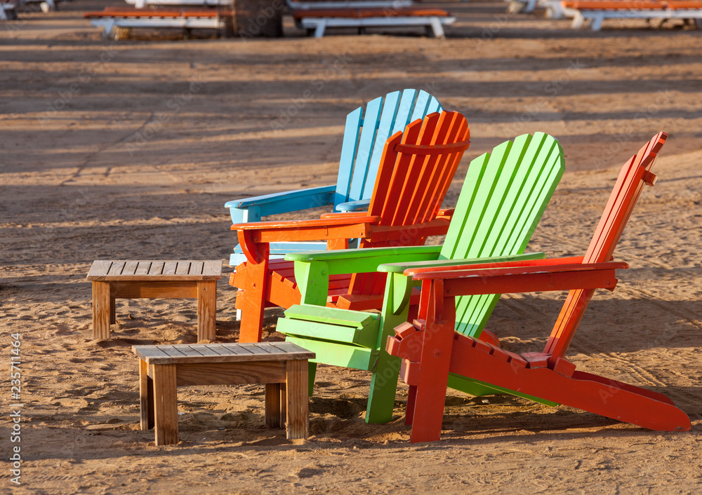 Multicolored wooden armchairs on the morning sandy beach.