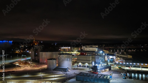 Modern grain terminal at night. Metal tanks of elevator. Grain-drying complex construction. Commercial grain or seed silos at seaport. Steel storage for agricultural harvest.