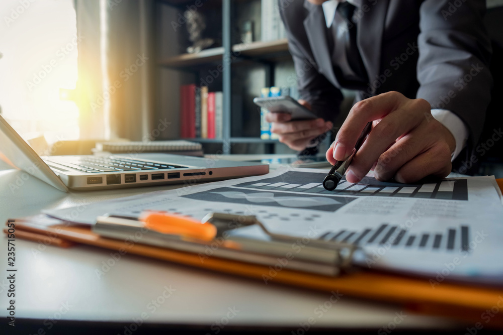 business documents on office desk with laptop and smart phone and graph business diagram and man working at office . business documents on office desk with laptop and smart phone and graph business diagram and man working at office .