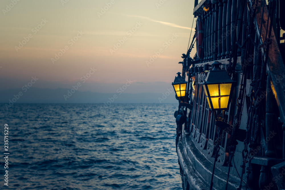 Naklejka premium stary drewniany statek piracki vintage na powierzchni wody morskiej w romantyczny wieczór o zachodzie słońca z żółtym światłem z miękkiej latarni w przestrzeni za burtą
