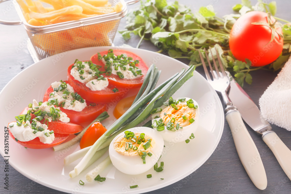 Half boiled eggs with tomatoes, green onions sprinkled with greens in a white plate on a gray wooden table. Close-up Half boiled eggs with tomatoes, green onions sprinkled with greens in a white plate on a gray wooden table. Close-up