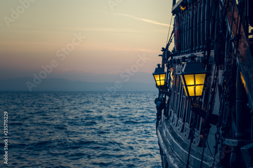 old wooden vintage pirate ship on sea water surface in sunset evening romantic time with yellow light from soft focus lantern in overboard space 