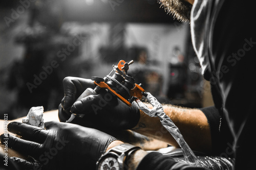 The tattoo artist creates a picture on the body of a man. close-up of tattoo machines and hands photo