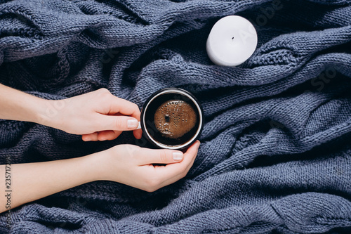 Winter or autumn cozy concept. Hand holds cup of coffee and candle on blue knitted sweater. Flat lay, top view.
