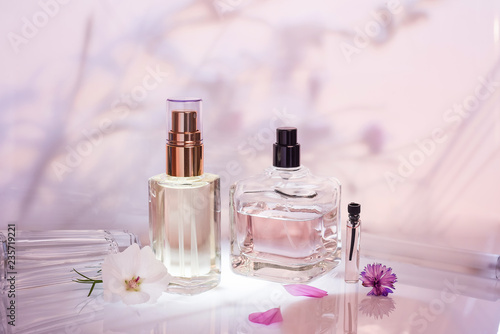 Different perfume bottles and sampler with plants on a pink floral background. Selective focus. Perfumery collection, photo