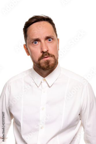 Portrait of handsome man with stubble has indignant expression, frowns face, dressed in white shirt, isolated over white background.