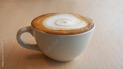 Hot coffee cappuccino latte in ceramic cup with spiral milk foam on plywood table background. photo
