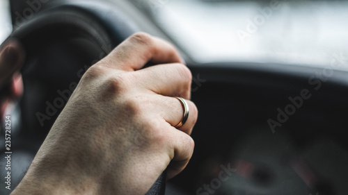 Men driver's hand with wedding ring on the steering wheel. Close up