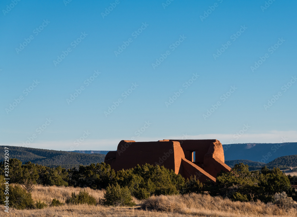 Fototapeta premium Ruins of an old adobe Spanish mission church set in a landscape of grassy meadows, trees, and mesas at Pecos National Historic Park near Santa Fe, New Mexico
