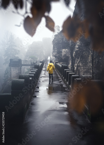 Wanderer auf der Basteibr  cke mit gelber Regenjacke bei Nebel und Regen