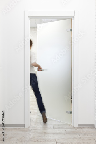 Person entering a room in office with minimalist white interior thru frosted glass door