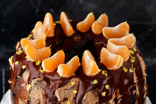 Dessert cake with chocolate icing decorated with tangerines on a black background.