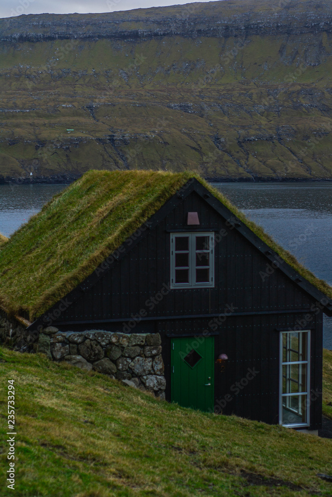 Obraz premium Scenic landscape view of traditional historic stone wooden house/building with grass (turf) roof in Gasadálur village, Vágar Island. Tourist popular attraction/place in Faroe Islands (Denmark)