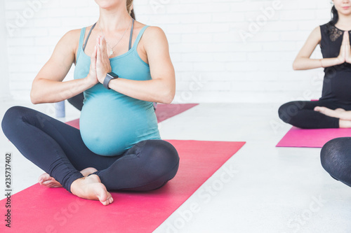 pregnancy, sport, fitness, people and healthy lifestyle concept - group of happy pregnant women exercising yoga and and meditating in lotus pose in white background gym