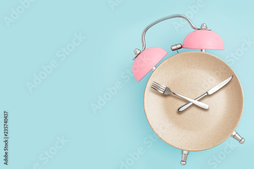 Alarm clock and plate with cutlery . Concept of intermittent fasting, lunchtime, diet and weight loss