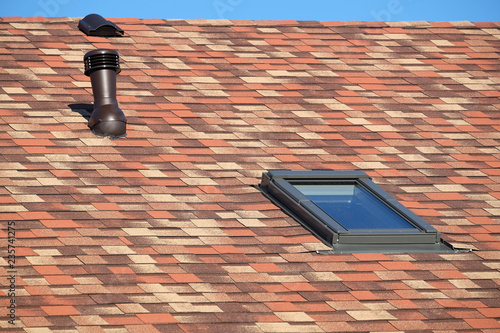 Roof window and ventilation tube on residential house covered with motley soft shingles close up view photo