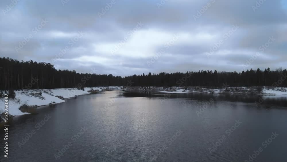 Aerial view. The lake in the winter forest. Flying over a not frozen lake in cloudy winter weather. Colorful landscape, frosty evening. Winter Russian nature. Lake surrounded by snow. 4K Aerial view. The lake in the winter forest. Flying over a not frozen lake in cloudy winter weather. Colorful landscape, frosty evening. Winter Russian nature. Lake surrounded by snow. 4K