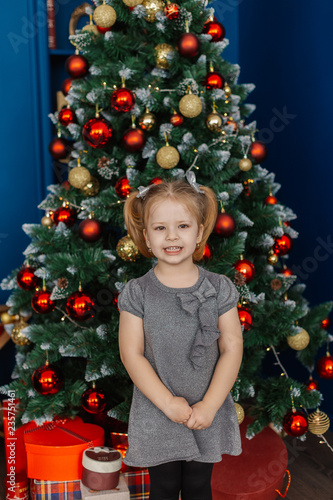 Very beautiful little girl standing at the Christmas tree with gifts.