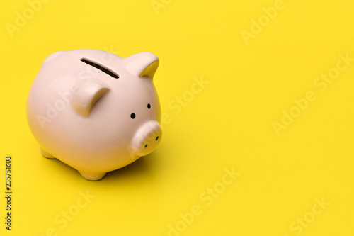 Pink piggy Bank stands on the left on a yellow background. On the right there is a place in copyspace