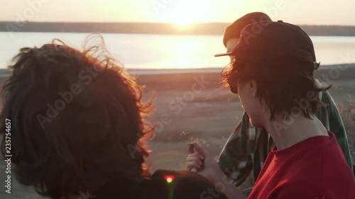 Three happy friends smoking joint at seashore at sunset rapid slow motion