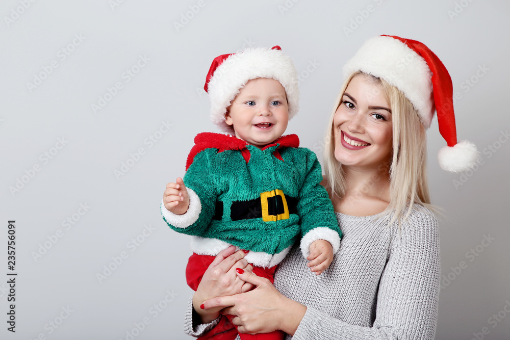 Mother and baby in santa hats on grey background Mother and baby in santa hats on grey background