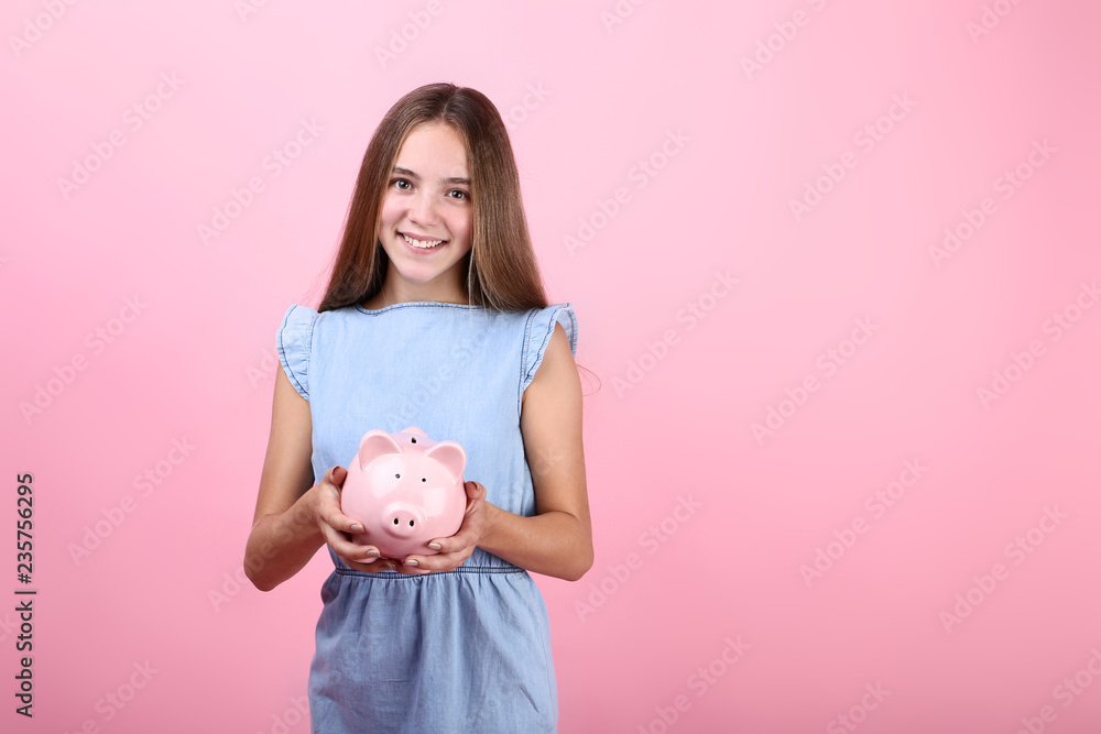 Young girl holding pink piggybank on pink background Young girl holding pink piggybank on pink background