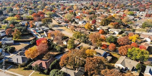 Panorama top view beautiful neighborhood in Coppell, Texas, USA in autumn season. Row of single-family home with attached garage, garden, surrounded by colorful fall foliage leaves under blue sky