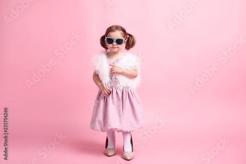 Beautiful little girl in fashion clothes on pink background