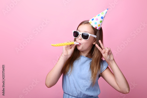 Cute young girl with birthday hat and whistle on pink background
