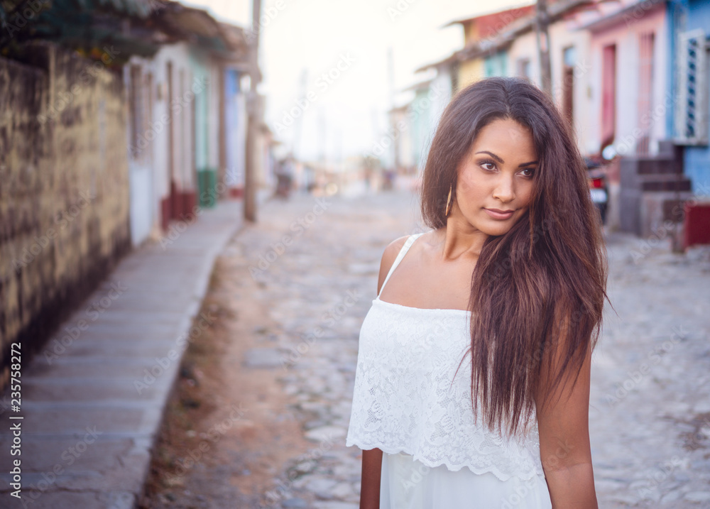 Beautiful dark skinned young lady in white dress standing in the old streets of Trinidad in Cuba.