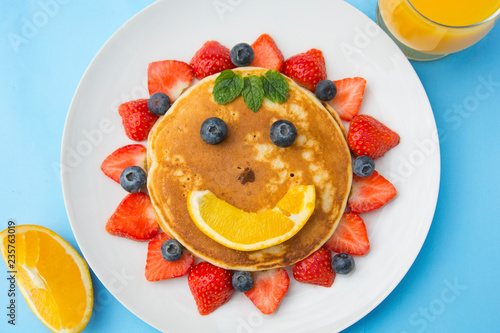 Breakfast for kids. Homemade american pancake sun, with fresh blueberries, strawberries and orange juice. Blue background.