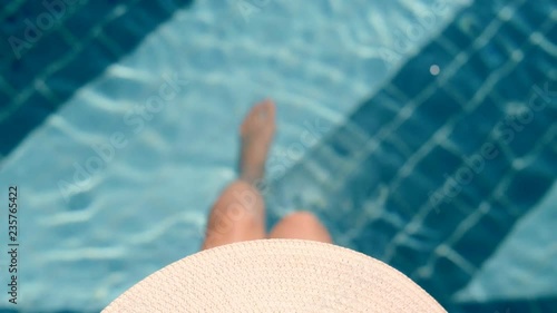 High angle playful young woman wearing hat relaxing in outdoor swimming pool at spa resort slow motion legs of attractive elegant female playing in clean pure water top view