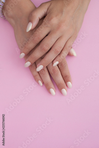 Tanned hands of a young woman with a light manicure on a pink background. Nail Polish