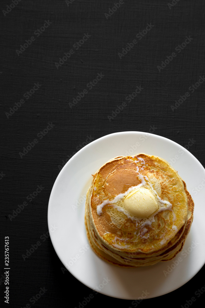 Homemade pancakes with butter on white plate over dark background, top view. Flat lay, overhead, from above. Copy space.