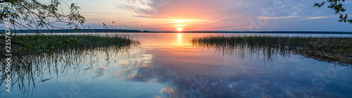 The rays of the dawn sun on the lake. Reflection of sunset clouds in the river. Rural landscape. Panoramic banner