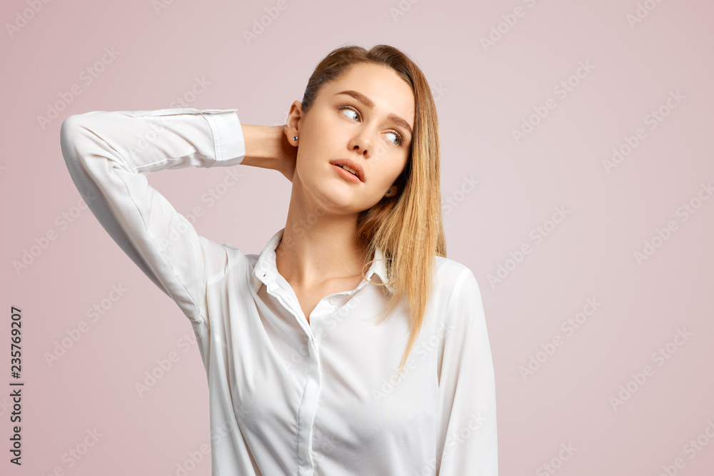 A student or office worker with long blonde hair in a shirt looking away with a serious facial expression. Beautiful woman posing isolated on pale pink Studio wall with copy space for your content