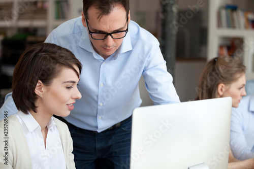Slika na platnu Middle aged serious mentor helping female employee with computer work, economic