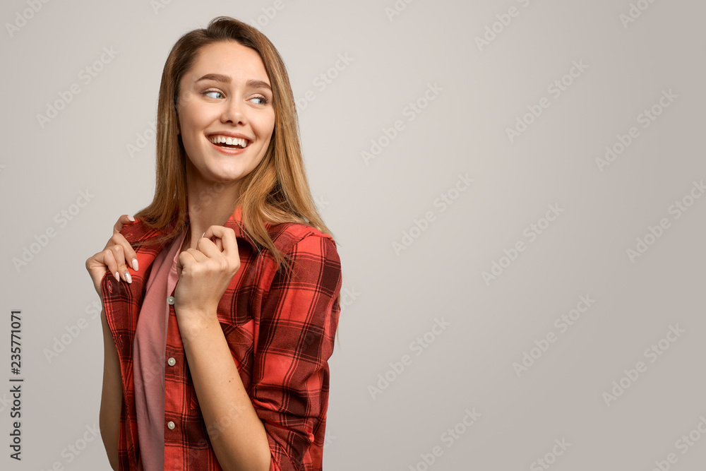 The girl in the red plaid shirt in the Studio. Beautiful girl with long blonde hair, has a toothy smile, looks happily to the side, waiting for a surprise from the guy. Isolated on white background The girl in the red plaid shirt in the Studio. Beautiful girl with long blonde hair, has a toothy smile, looks happily to the side, waiting for a surprise from the guy. Isolated on white background