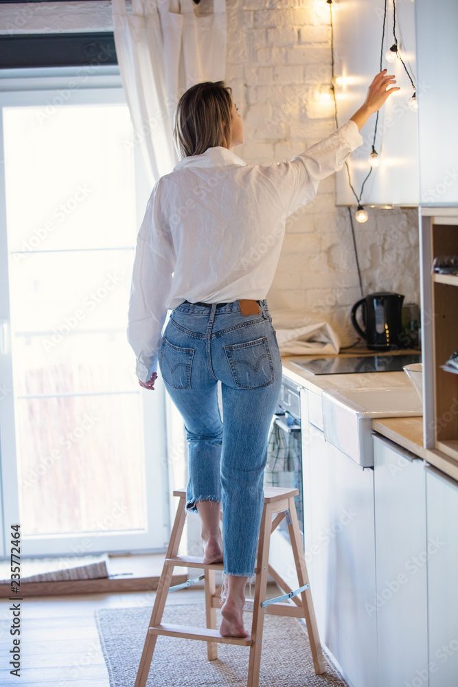 Young caucasian woman in white shirt and blue jeans stay on kitchen.