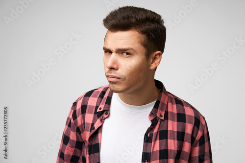 Attentive young man looks suspiciously standing in a half-turn as if he is peeping or overhears, has an incredulous look, isolated over white background photo