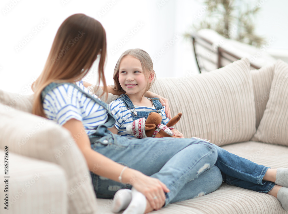 mom and little daughter sitting on the couch in a cozy living room mom and little daughter sitting on the couch in a cozy living room